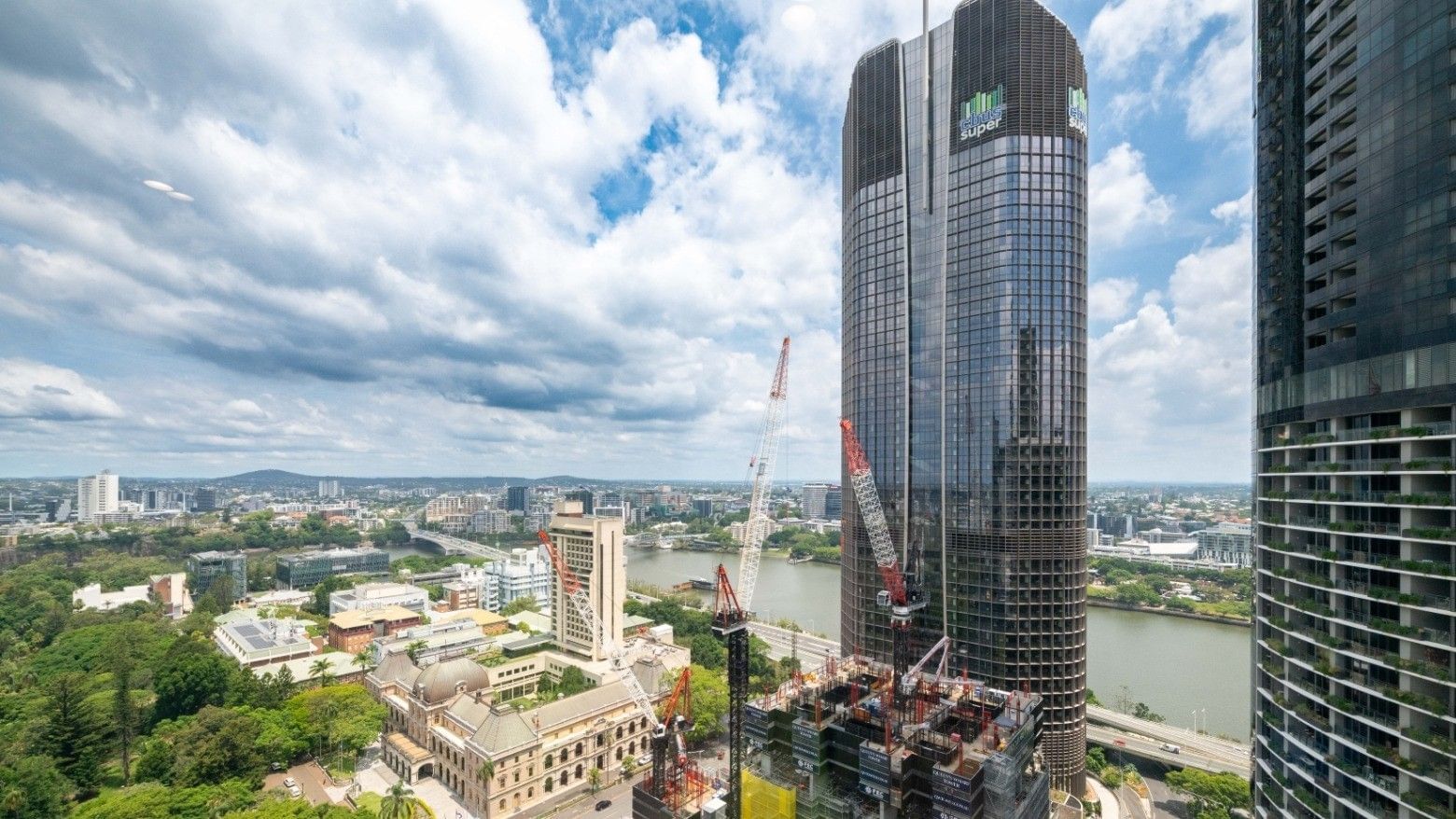 Tall skyscraper under construction with cranes near river and cityscape at UniLodge Brisbane City.