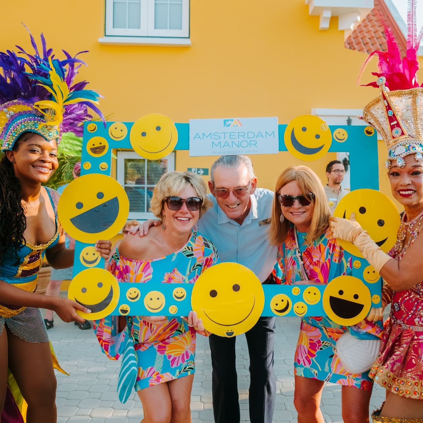 Group of people dressed in festive costumes hold a sign with smiley faces, celebrating International Day of Happiness at Amsterdam Manor.