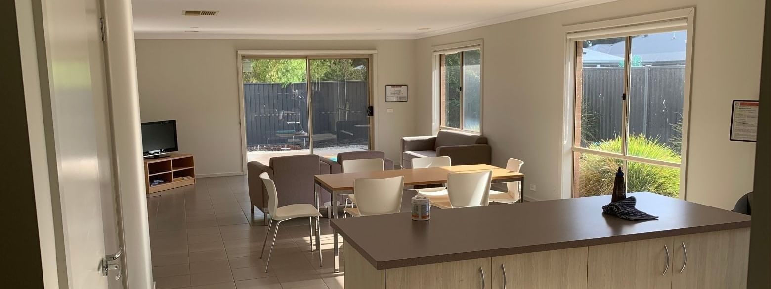 Open-plan living room with dining area, kitchen island, and sliding glass doors leading to the backyard.