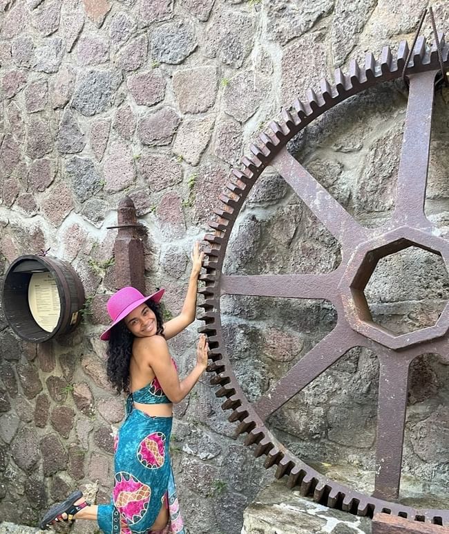 A person poses next to a large, rusted gear wheel mounted on a stone wall at Ladera Resort
