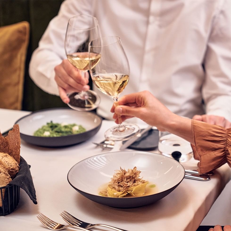 Coppie che brindano con vino bianco e gustano cibo gourmet durante le cene di vino 2026.