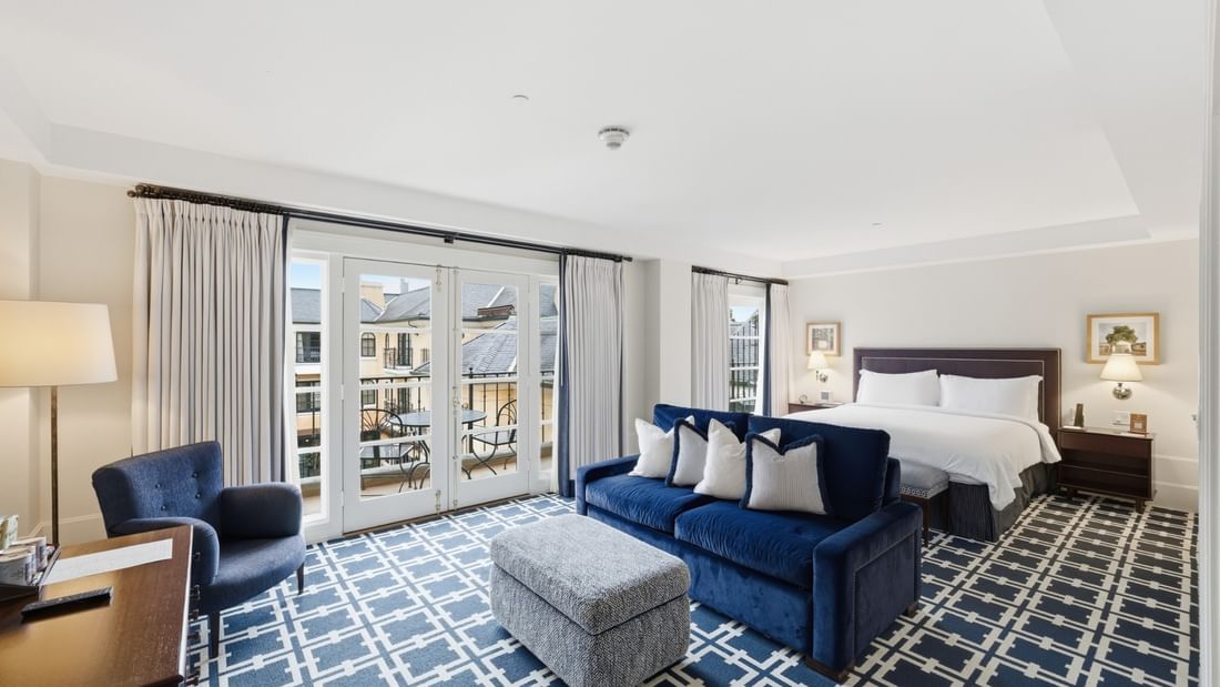 Spacious Courtyard Grand Executive King Suite with blue sofa, patterned carpet, and balcony at el PRADO Hotel.