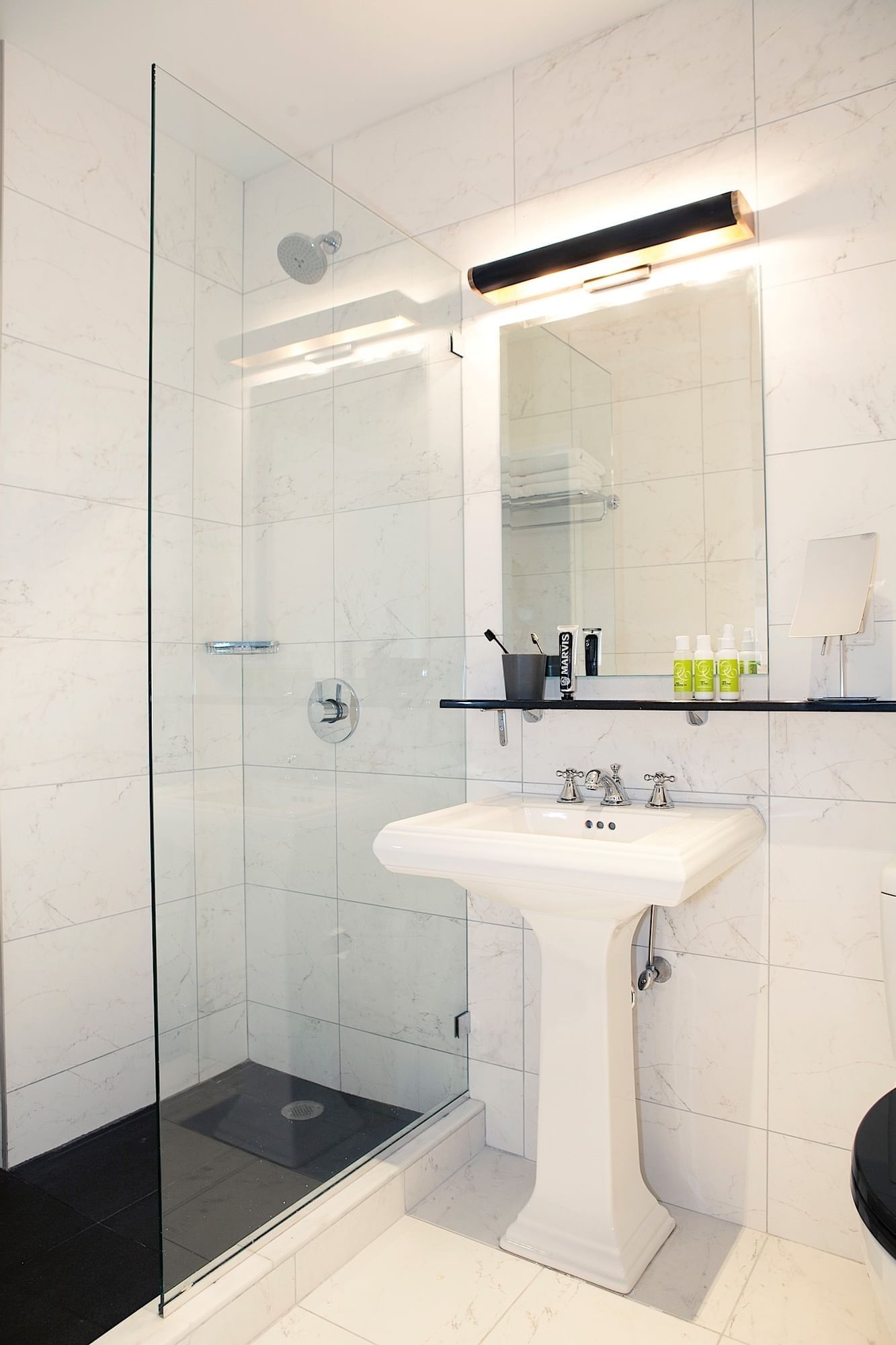 A clean bathroom with a glass-enclosed shower, pedestal sink, and marble tiles.