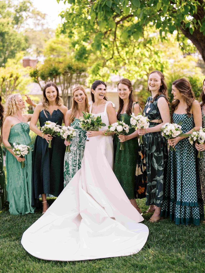 Bride and bridesmaids in green dresses holding floral bouquets, smiling and posing at The Clifton Hotel in Charlottesville.