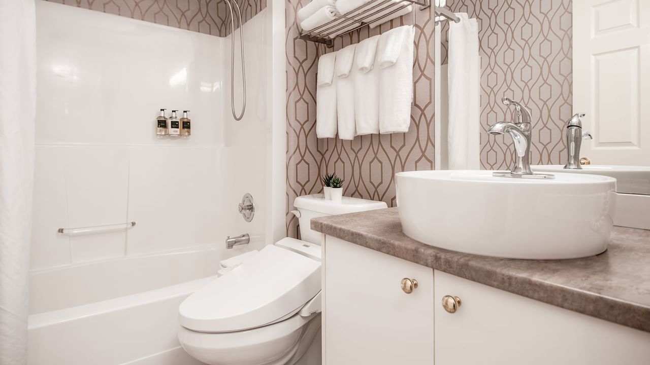 Hotel washroom with toilet, bathtub, sink, towels, and soap