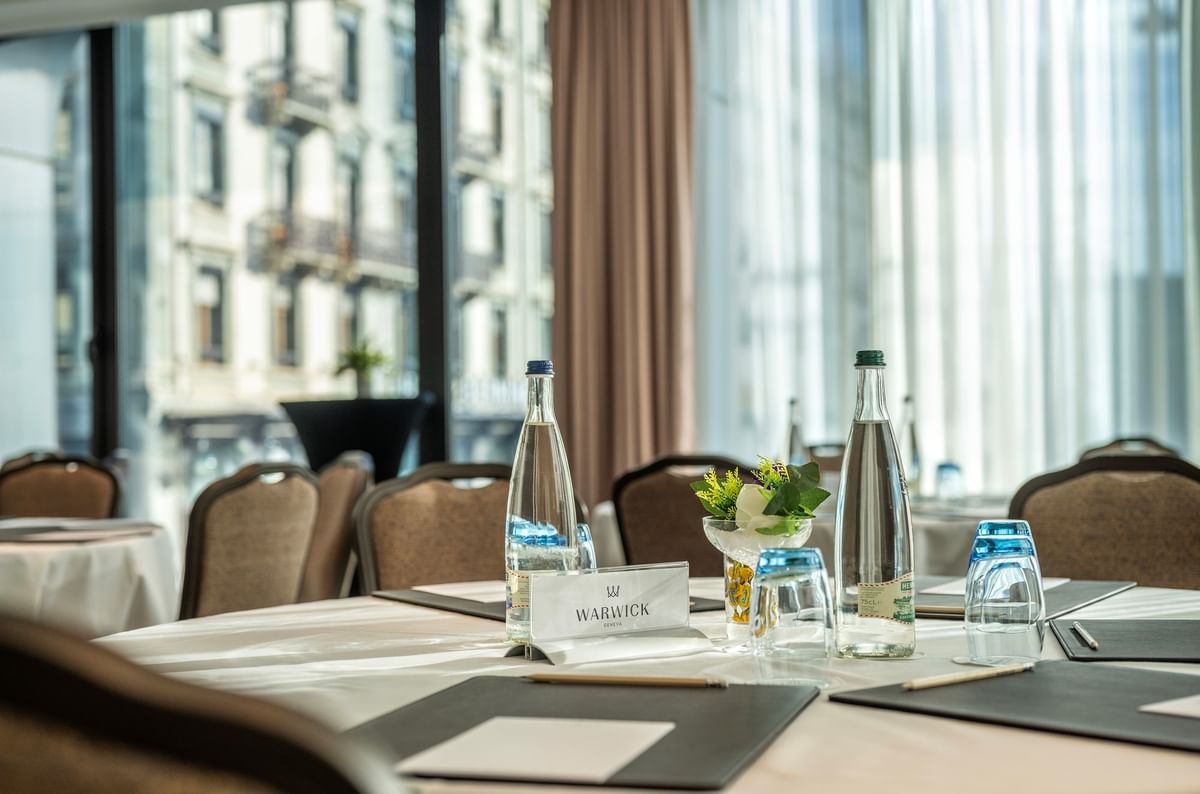 Bottled water and pads with pencils on a white cloth table by windows overlooking the city at Warwick Corporate