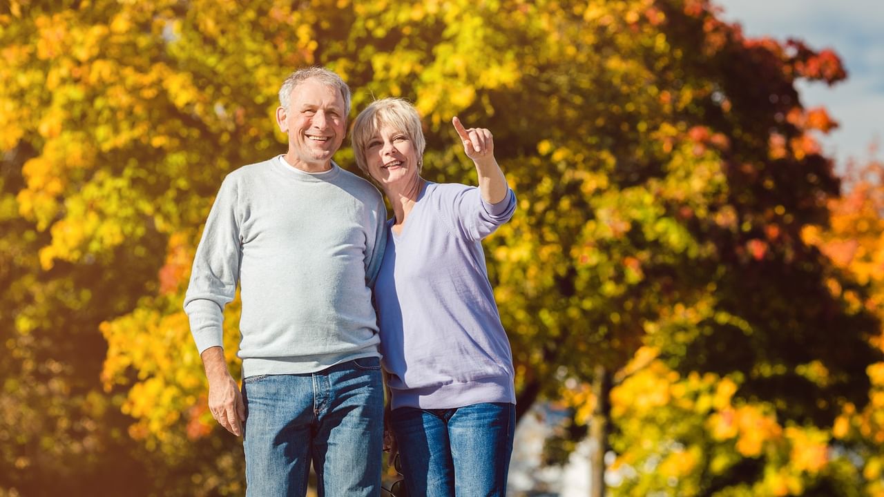 Senior couple outdoors with fall foliage one pointing