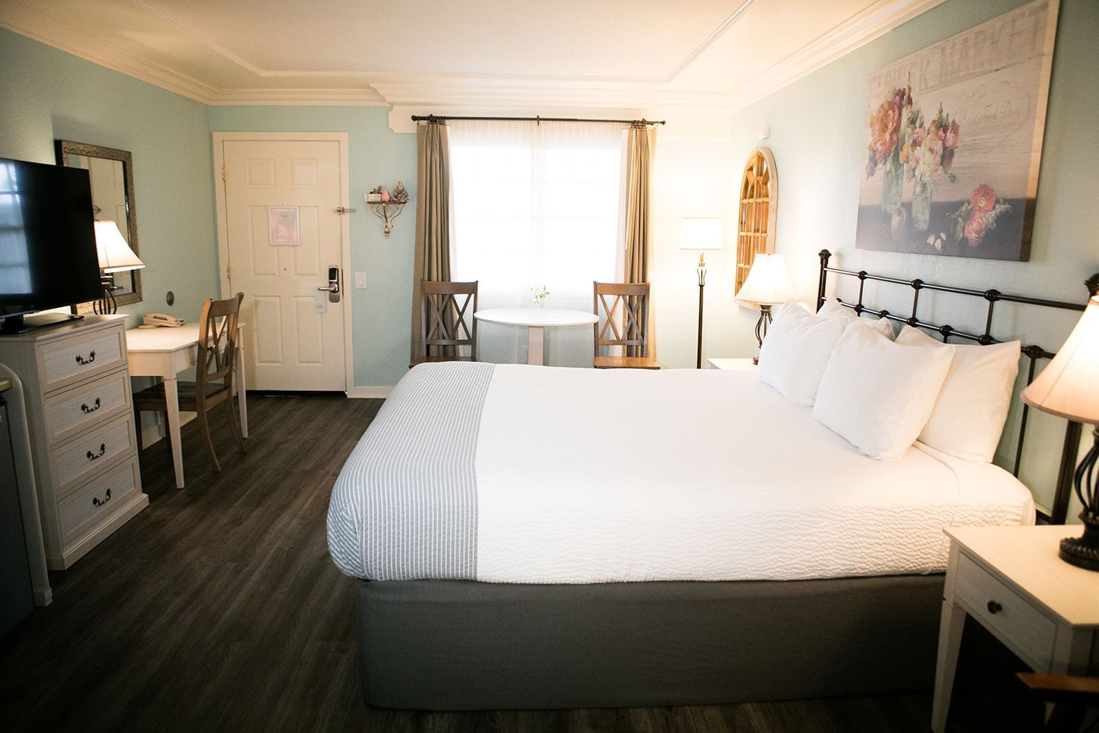 A wide view of a hotel room with a king-sized bed, desk, TV, and window.