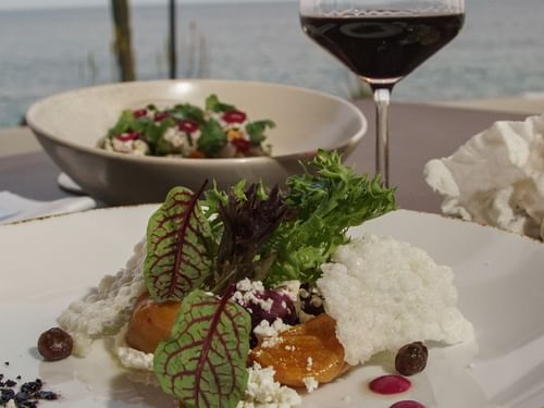 Dos ensaladas y una copa de vino tinto en una mesa con vista al mar en el restaurante Pitahayas de Hacienda del Mar Los Cabos.