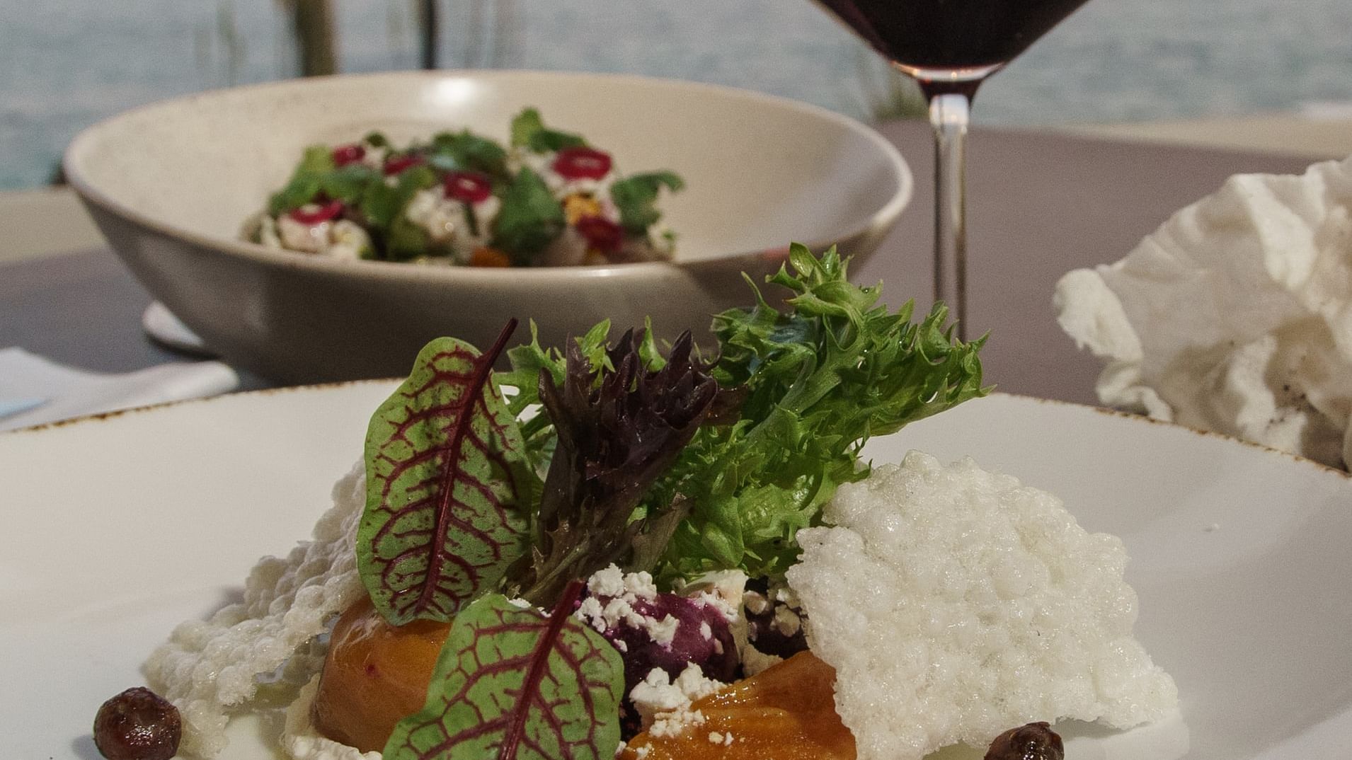 Dos ensaladas y una copa de vino tinto en una mesa con vista al mar en el restaurante Pitahayas de Hacienda del Mar Los Cabos.