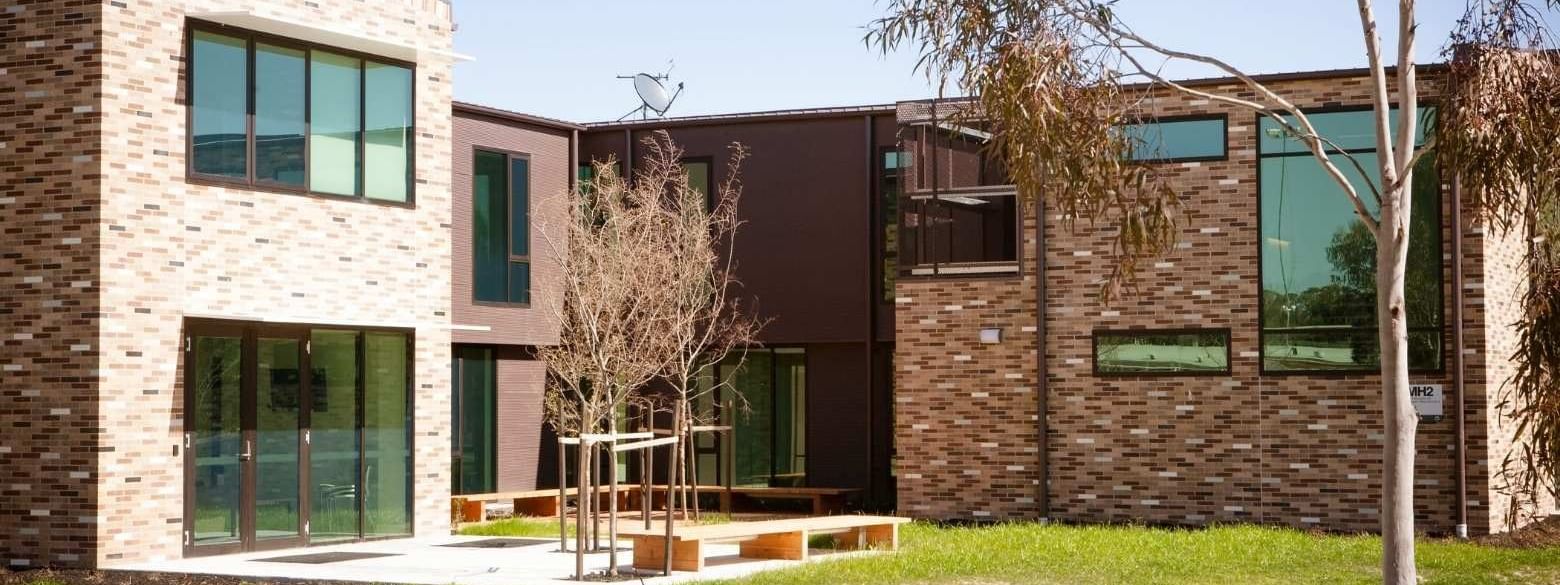 Modern brick building with glass windows, outdoor seating, and grassy yard with trees.