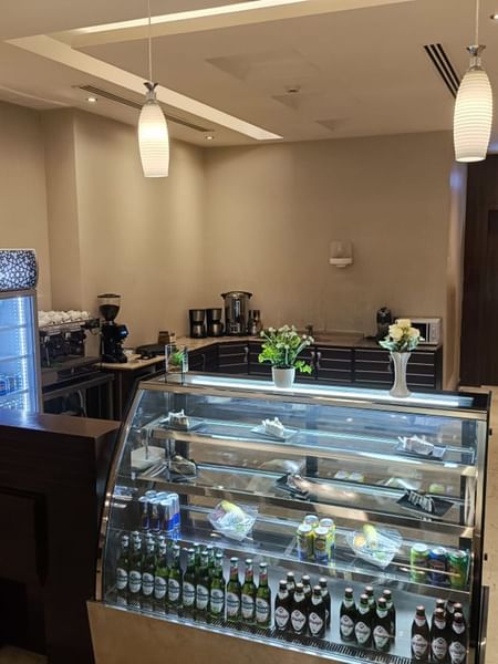 Coffee Shop with a glass display case under hanging lamps by a coffee machine at Naviti by Warwick Al Khobar
