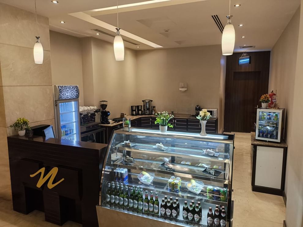 Coffee Shop with a glass display case under hanging lamps by a coffee machine at Naviti by Warwick Al Khobar