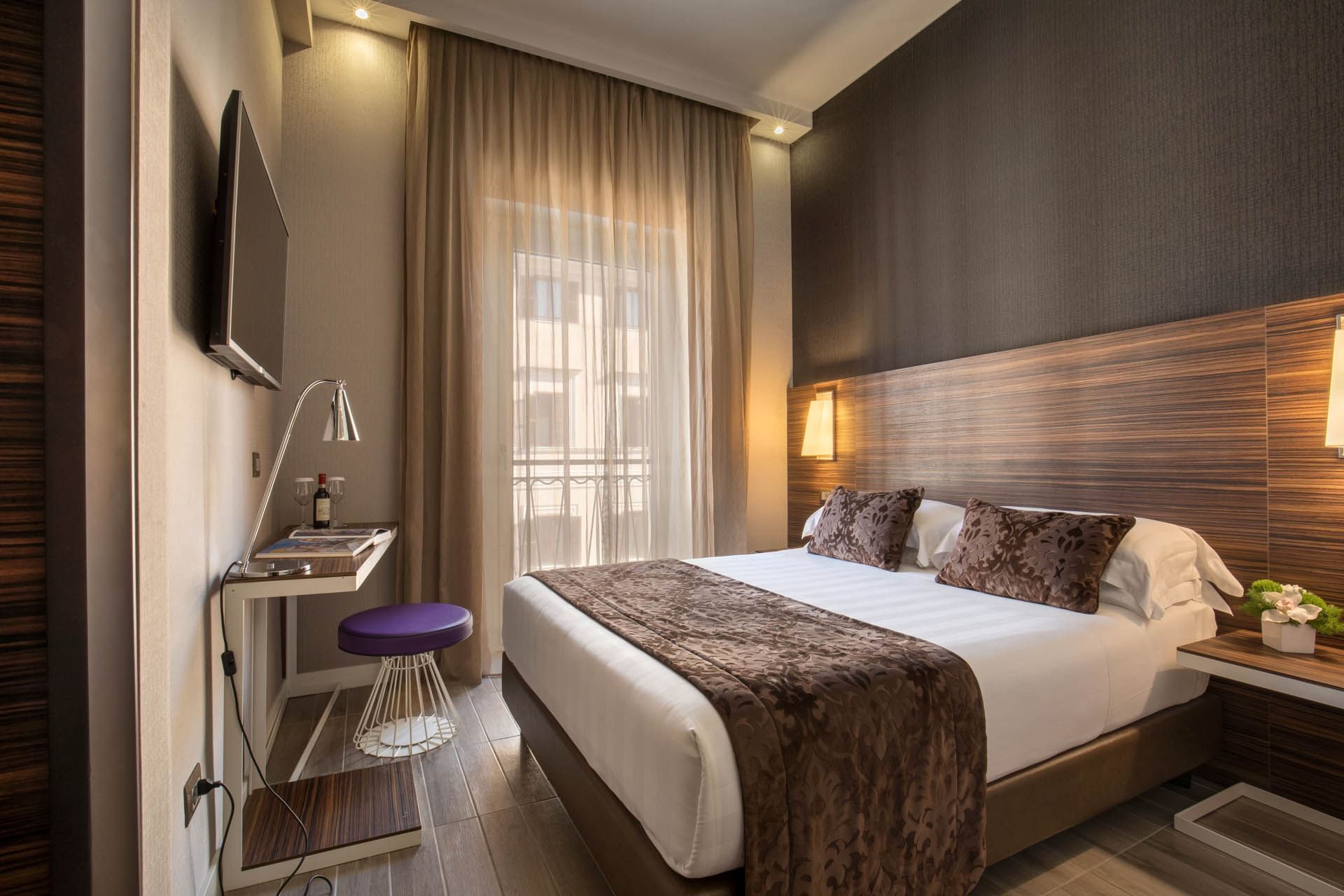 Deluxe Room with a queen bed, a desk, purple stool, TV, and sheer curtains allowing natural light at The Republic Hotel