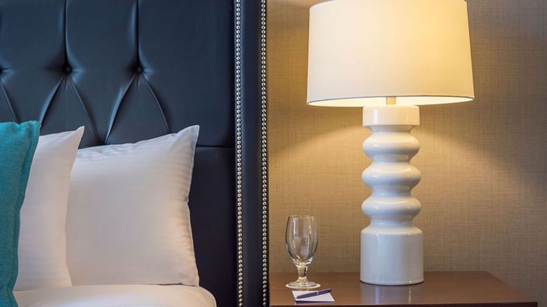 White lamp featuring a tiered base by a glass on a wooden nightstand in Queen Anne Suite at Warwick Seattle
