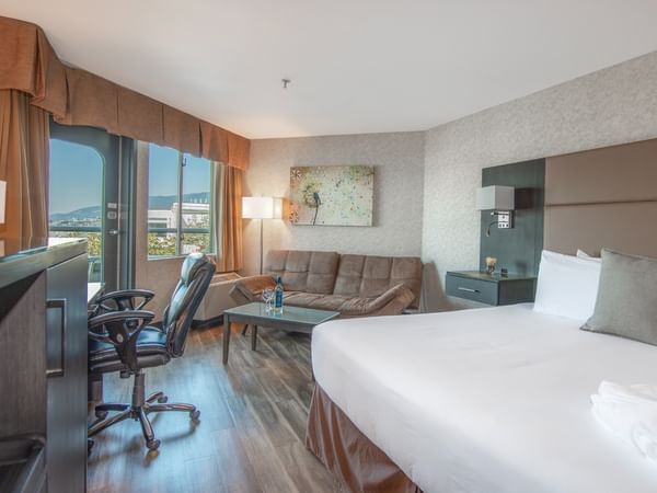 Coast Premium King with Patio with large bed, couch, chair, desk, TV, and scenic window view at Coast Lonsdale Quay Hotel