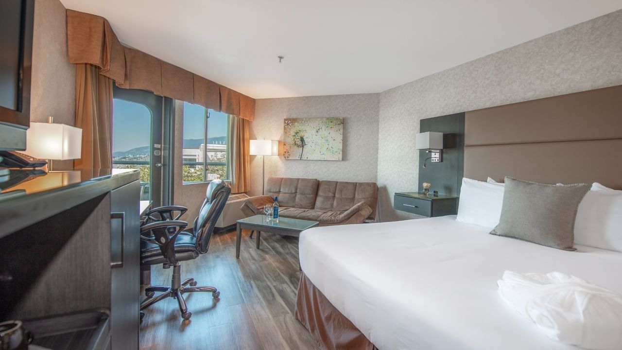 Coast Premium King with Patio with large bed, couch, chair, desk, TV, and scenic window view at Coast Lonsdale Quay Hotel