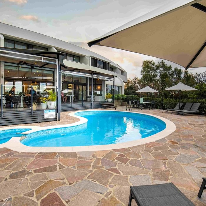 Pool area with stone tiles, lounge chairs, and umbrellas at Mercure Charlestown.
