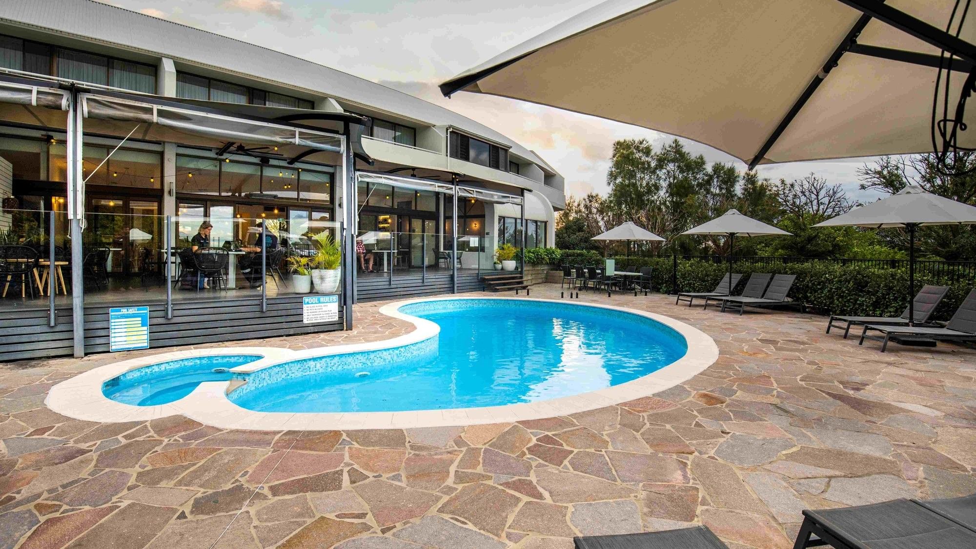 Pool area with stone tiles, lounge chairs, and umbrellas at Mercure Charlestown.