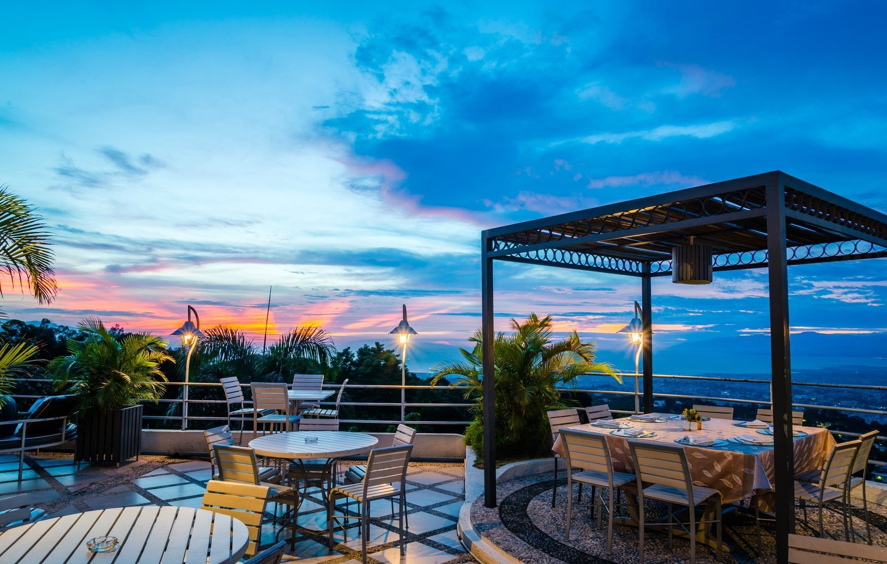 Outdoor terrace dining area with pergola and seating overlooking city views at sunset at Hotel Montana Haiti