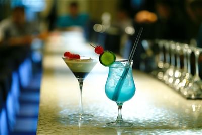 Two colorful cocktails on a bar counter, one blue and one martini glass with cherries at Hotel Mykonos