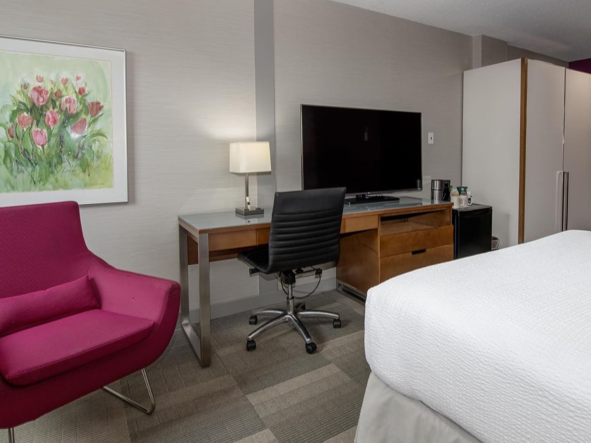 Coast Queen room with modern desk, pink accent chair, flat-screen TV, and white bedding at Coast Prince George Hotel