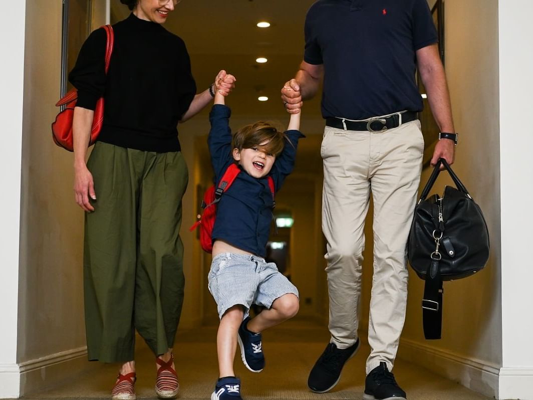 Couple holding hands with a child walking down a hallway at Nesuto The Entrance Apartments