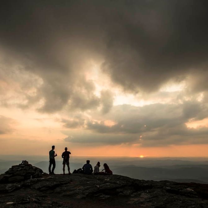 Hikers silhouetted against a stunning sunset on a mountain peak in Vermont.