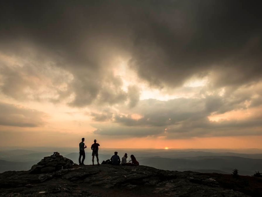 Hikers silhouetted against a stunning sunset on a mountain peak in Vermont.
