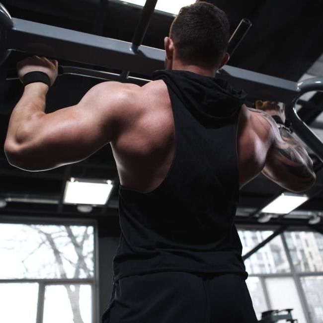 Person performing a pull-up exercise on a bar in a modern gym with large windows and industrial ceiling beams