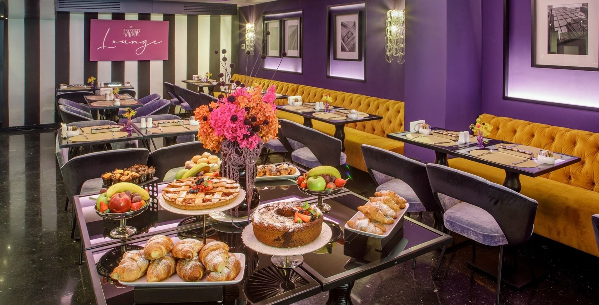 Elegant dining lounge at Tribune Hotel Rome with vibrant décor, velvet seating, and buffet breakfast offering fresh pastries, fruit, and cakes.