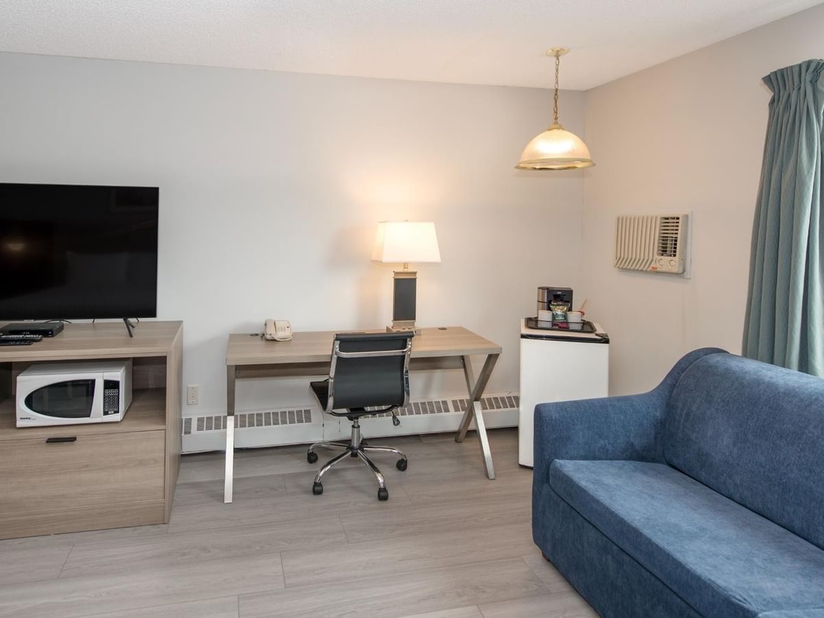 Room with blue couch, desk with chair, TV, microwave, lamp, and window with curtain.