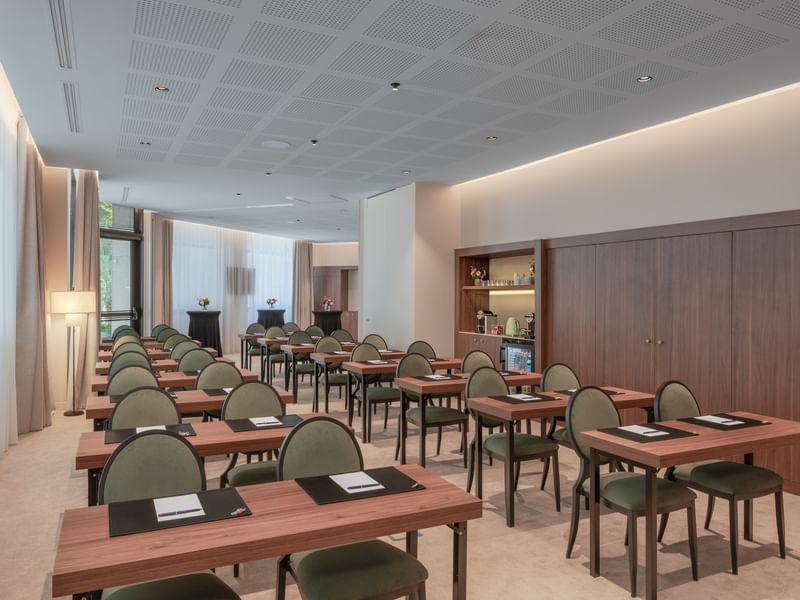 Empty conference room with rows of desks, chairs, and a wooden cabinet with shelves.