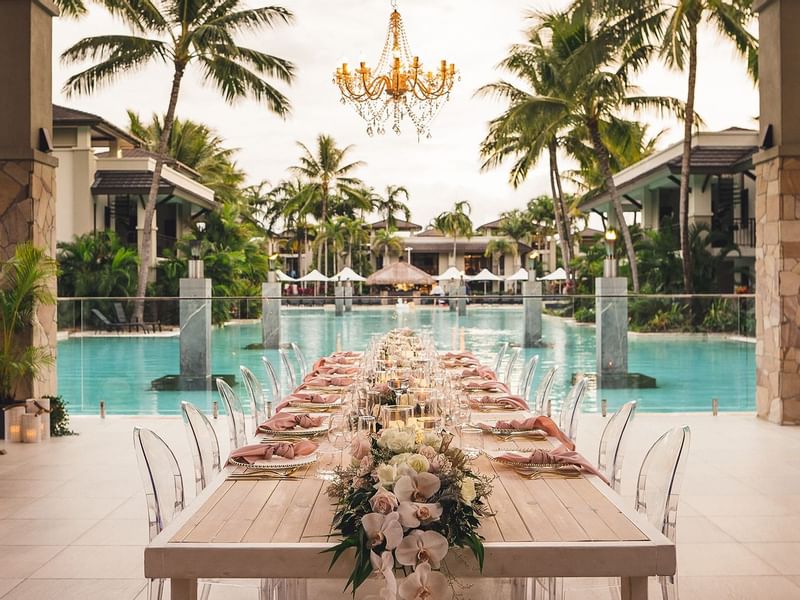 Outdoor dining setup adorned with flowers and a chandelier by the pool at Pullman Port Douglas
