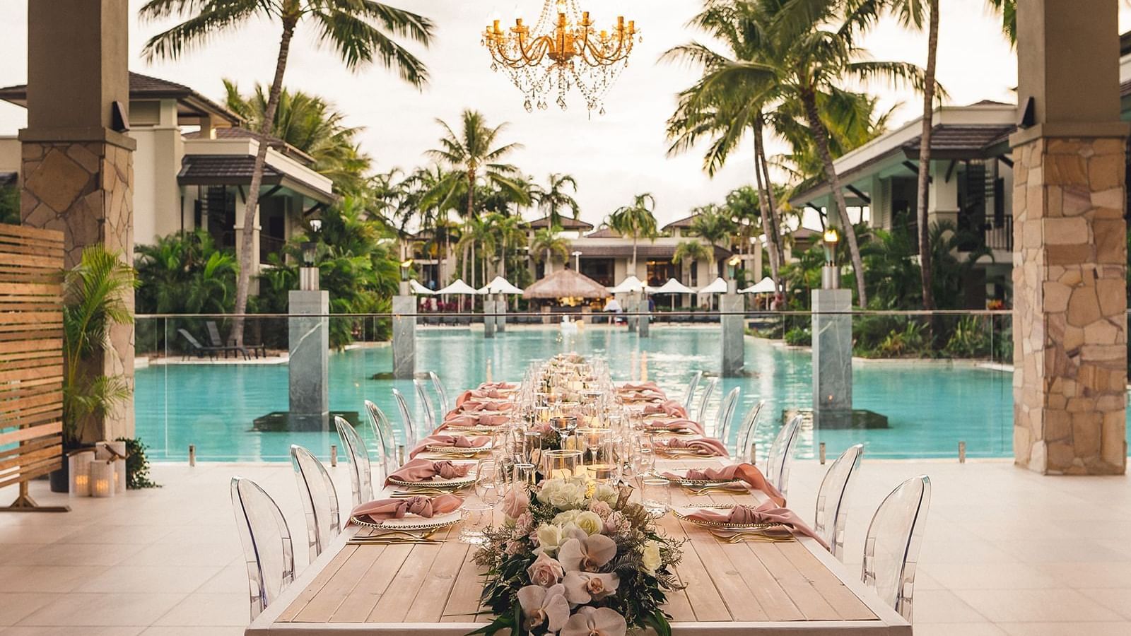 Outdoor dining setup adorned with flowers and a chandelier by the pool at Pullman Port Douglas