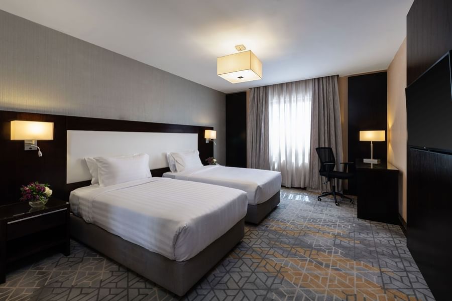 Nightstands and a work desk by the cozy beds in the Family Suite with carpeted floors at Warwick Hotel Jeddah