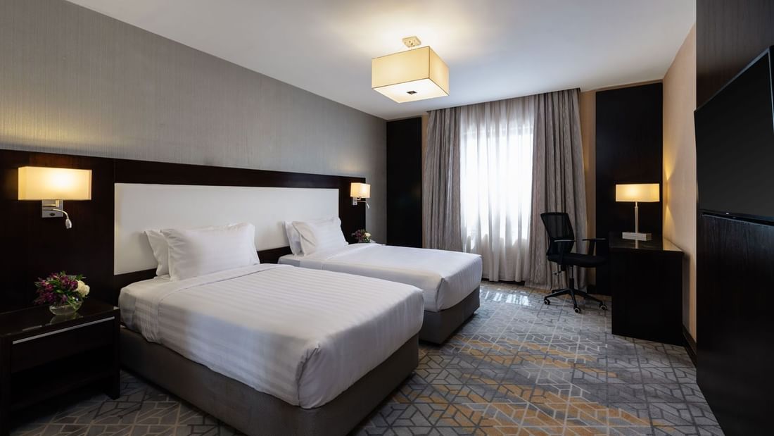 Nightstands and a work desk by the cozy beds in the Family Suite with carpeted floors at Warwick Hotel Jeddah