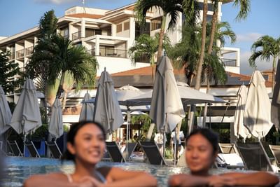 Two guests relax in the swimming pool, with lounge chairs and closed umbrellas at the Maui Coast Hotel