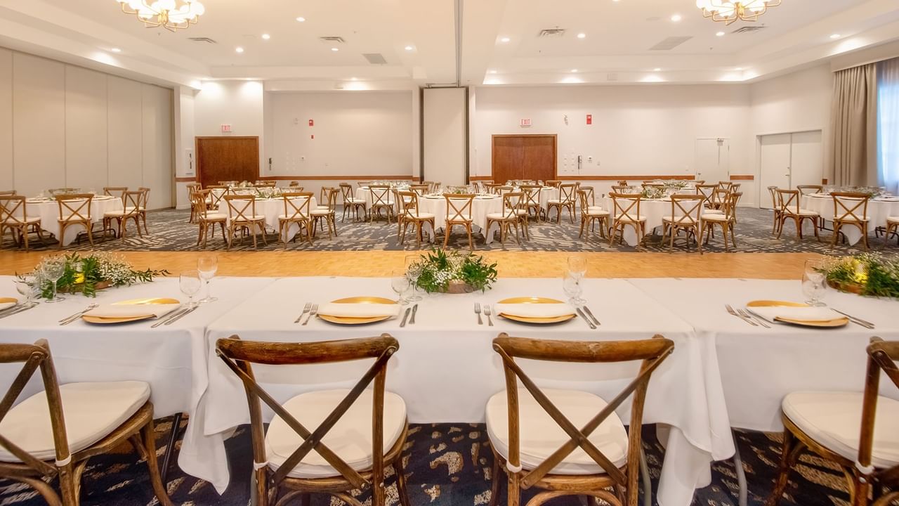 A large banquet hall with set tables and chairs, floral arrangements, and a carpeted floor.