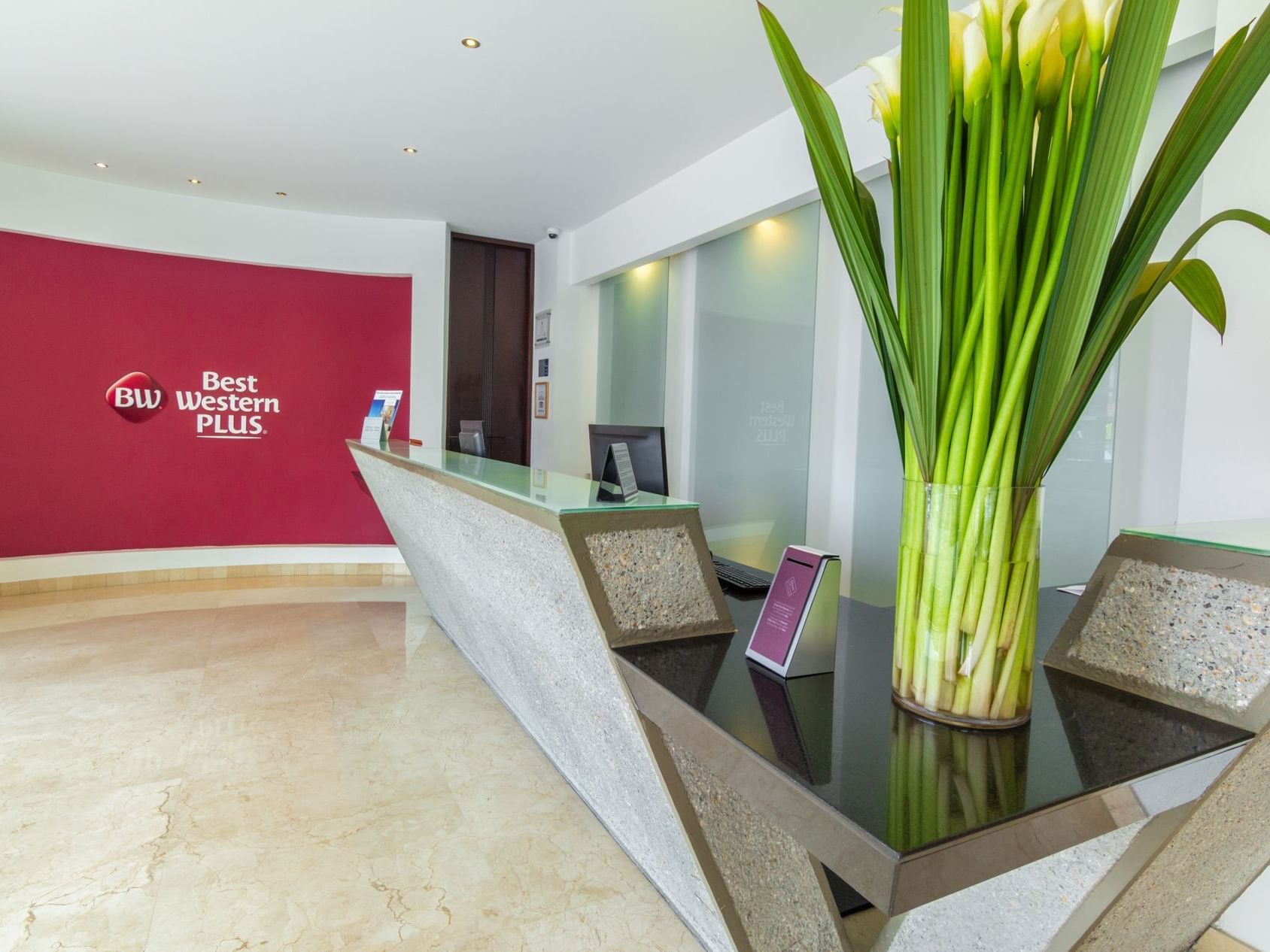 The reception area of the hotel with a marble table top, a computer and a plant on the side of the tabletop