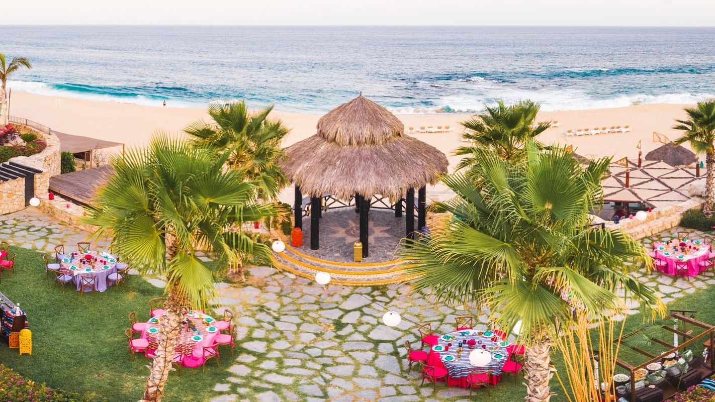 Aerial view of a scenic beach wedding setup at Hacienda del Mar Los Cabos with a palapa, tables, and ocean view