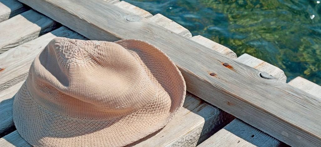Light-colored woven sunhat resting on a wooden dock beside clear water.