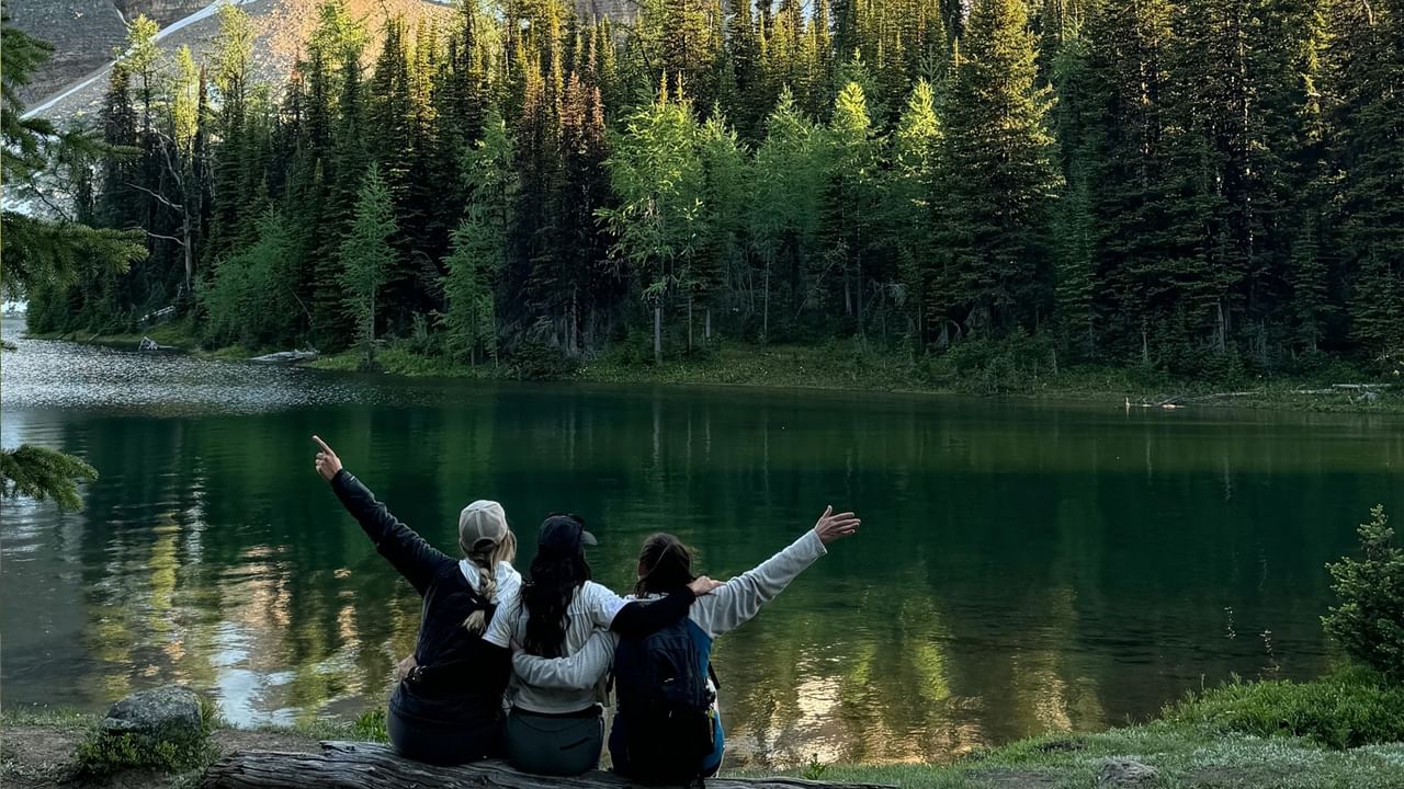 Three friends take a picture together at the side of a lake in Banff.