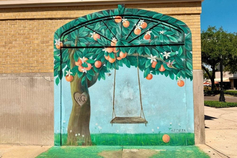 An arched mural on a wall of a wooden swing hanging from an orange tree. 