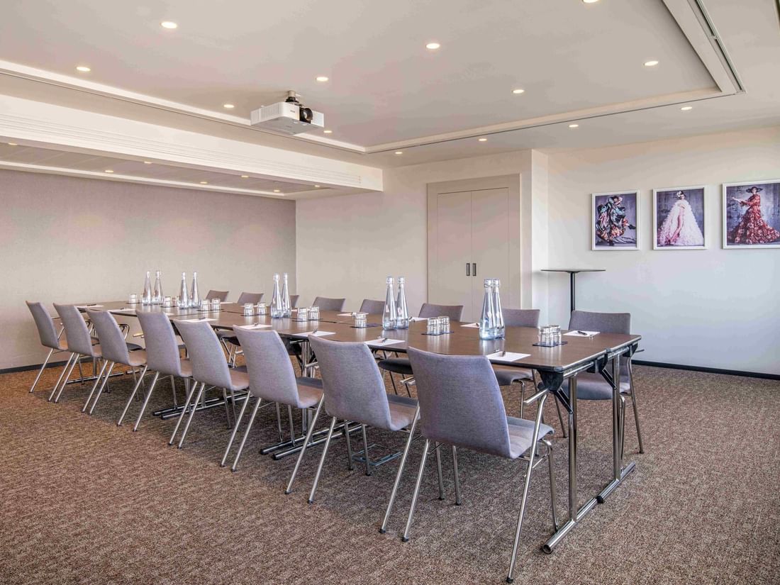 Meet 25 One Meeting room with a long table, chairs, water bottles, and framed artwork on the wall at The Hotel Brussels