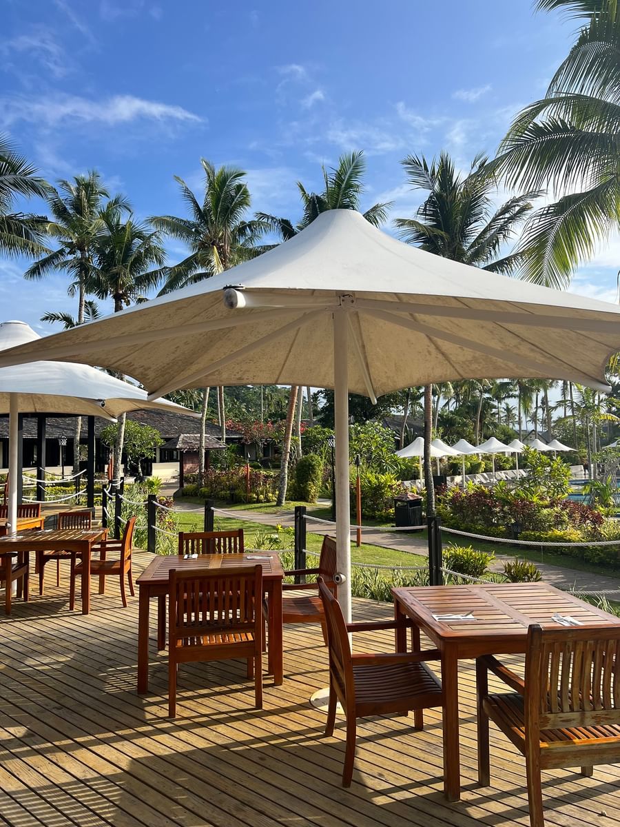 Outdoor dining area with umbrellas and wooden tables and chairs at Warwick Le Lagon - Vanuatu.