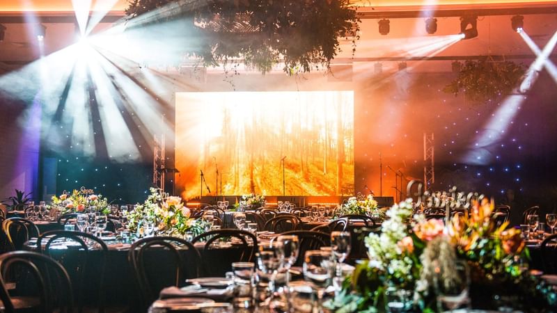 Set up banquets adorned with flowers facing a large screen in Minyama room at Novotel Sunshine Coast Resort