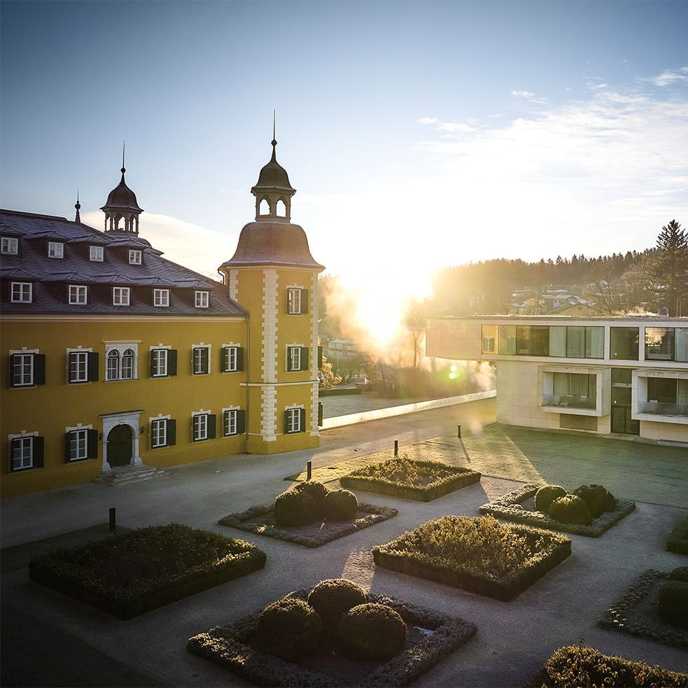 Sonnenaufgang über einer gepflegten Gartenanlage mit historischem und modernem Gebäude.