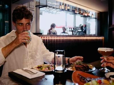 Man drinking from a glass and enjoying his dinner in The Reserve Restaurant at Amora Hotel Riverwalk Melbourne