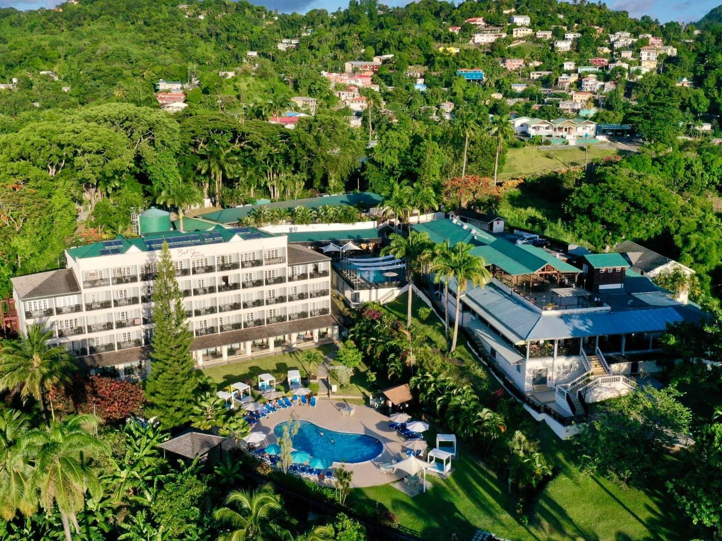 Aerial drone view of a hillside tropical Bel Jou Hotel featuring a white multi-story building and a blue swimming pool